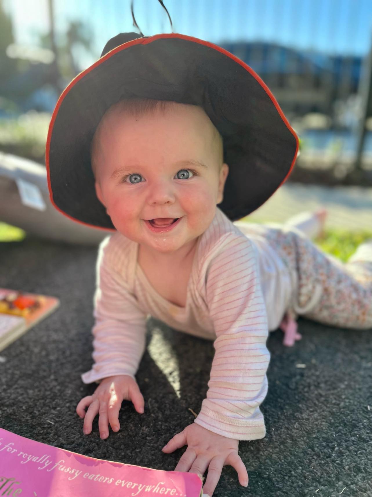 Smiling baby wearing a sun hat crawling on the ground outdoors during playtime, learning and exploring the world.