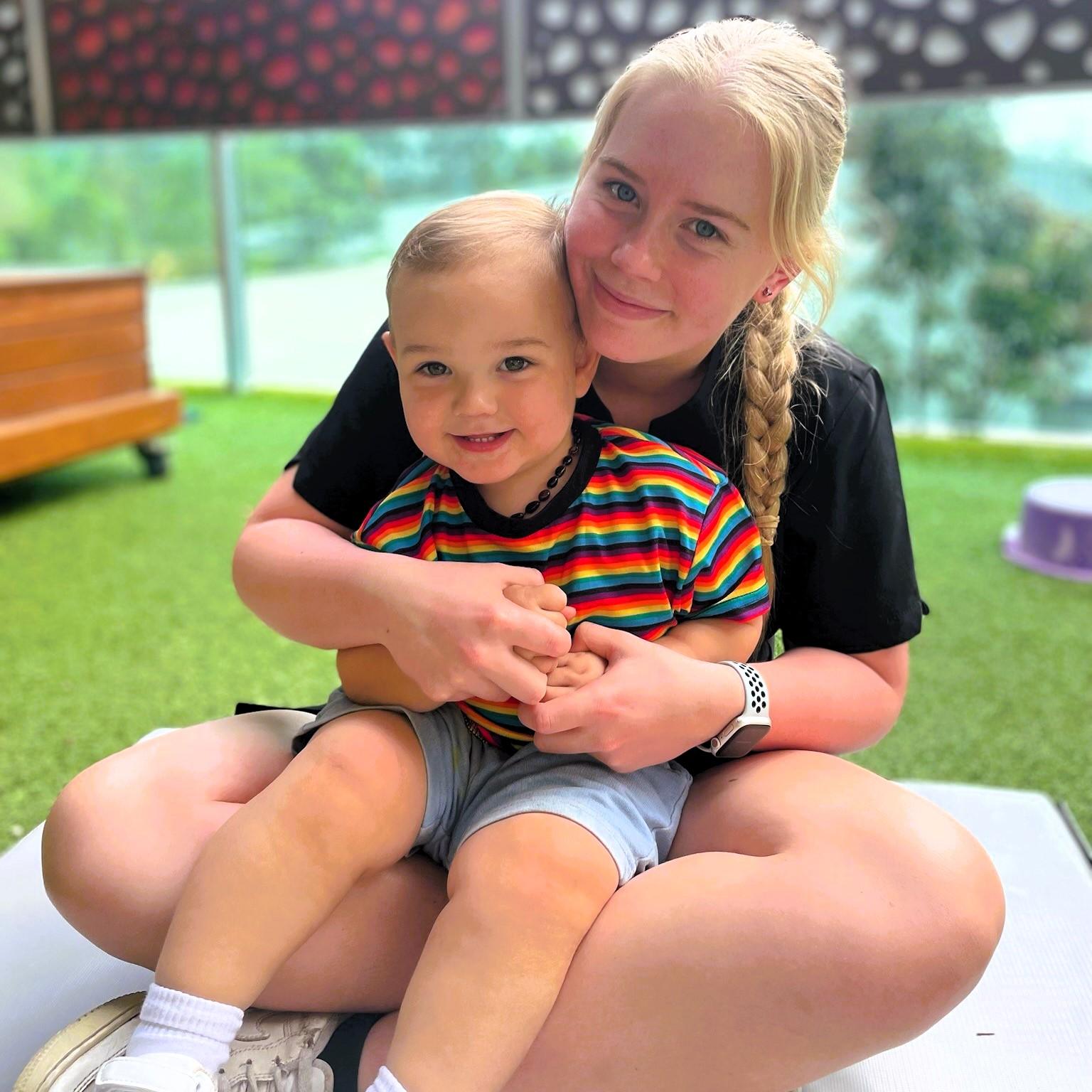 Smiling Little Scholars educator hugging a toddler in a striped shirt, showcasing the caring and nurturing relationship between staff and children.